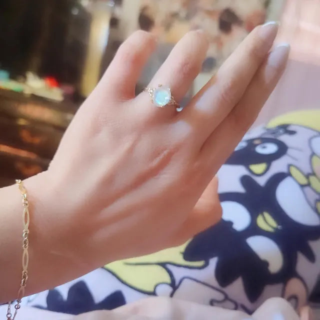 Hand wearing a gold ring with a gemstone, with a colorful background